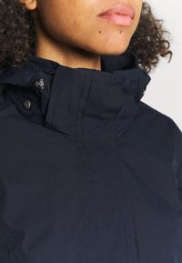 Chaqueta azul marino con cuello alto, botones a presión y detalles de costura visibles. Textura suave con un diseño minimalista.