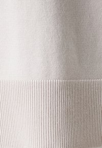 Lys beige strikket stoff med en glatt tekstur, med en ribbestrikket kant nederst. Designet er enkelt og jevnt gjennom hele.