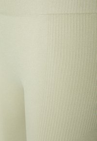 Leggings verde claro com uma textura suave e detalhes en ribetes, apresentando um design ajustado e um tecido elástico para conforto.