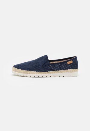 Navy slip-on shoe with perforated fabric, cream braided sole, and textured accents. Features a subtle logo near the heel.