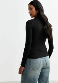 Svart åtsittande långärmad topp med ribbad textur, rundad nederkant och vågiga kanter, matchad med ljusblå högmidjade jeans.