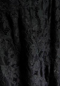 Svart spets tyg med blommönster, som har intrikata detaljer och en mjuk textur, vilket skapar en lager-på-lager, genomskinlig look.