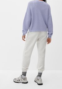 Levandulový pletený svetr s texturovaným vzorem, zkombinovaný s off-white žebrovanými joggery. Obuv je zdobena šedými a černými akcenty s grafickými ponožkami.