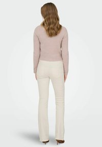 Light pink knitted sweater with long sleeves, paired with cream-colored flared jeans. Model wears brown high-heeled shoes.
