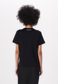 Tricou negru cu mânecă scurtă și guler rotund, realizat dintr-un material neted. Dispune de logo-ul alb "KARL LAGERFELD" pe spate.