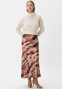 Beżowy sweter golf z długą, zwiewną spódnicą w różowy, czarny i beżowy abstrakcyjny wzór; noszony z jasnobrązowymi botkami za kostkę.