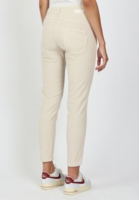 Beige trousers with a fitted design, featuring back pockets and a textured fabric. Paired with white sneakers accented in red.