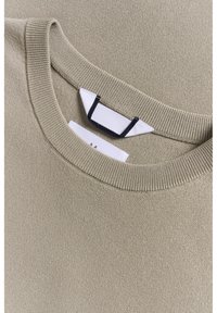 Beige pletený svetr s kulatým výstřihem, žebrovanými detaily a textilní etiketou s černými akcenty na vnitřním límci.