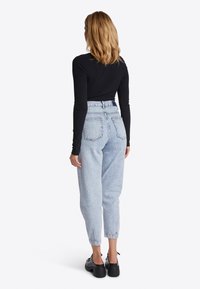 Zwarte geribbelde langemouwen top gecombineerd met lichtblauwe high-waisted denim jeans. Soepele textuur; de jeans hebben vier zakken en zijn voorzien van omgeslagen boorden.