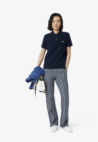 Laivastonsininen polo-paita lyhyillä hihoilla ja kauluksella, yhdistettynä geometrisia kuvioita sisältäviin kuvioituihin housuihin, valkoisiin lenkkarikenkiin ja pieneen valkoiseen laukkuun.