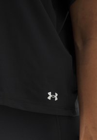 Svart treningsgenser med løs passform, jevn tekstur og en sølvfarget Under Armour-logo nær kanten. Ingen distinkte mønstre eller detaljer.