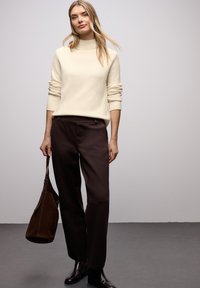 Kremowy sweter z golfem, miękka faktura, prążkowane mankiety. Ciemnobrązowe spodnie z wysokim stanem, dopasowany krój. Brązowa zamszowa torebka na ramię, gładkie wykończenie.