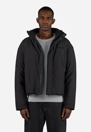 Black puffer jacket with a hood, zip front, and side pockets. Features a textured gray sweater underneath and dark jeans. Simple, modern design.
