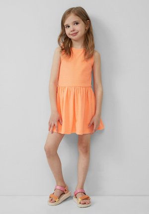 Kurzes oranges Kleid mit tailliertem Oberteil und ausgestellt Rock. Strukturierter Stoff und ärmelloses Design. Sandalen mit mehrfarbigen Riemen und flacher Sohle.