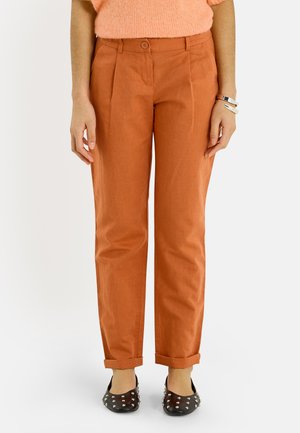 Pantalones de pierna recta color óxido con dobladillos remangados, usados con zapatos planos negros con tachuelas y una camiseta de manga corta suave color durazno en una persona de pie.