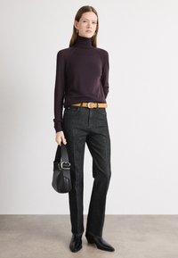 Pull à col roulé violet foncé à manches longues, associé à un jean droit gris foncé, une ceinture beige et un petit sac à main noir.