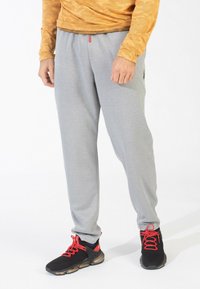 Grå sweatpants med elastisk talje, sidelommer og et lille logo. Båret sammen med sorte sneakers med røde snørebånd og detaljer.