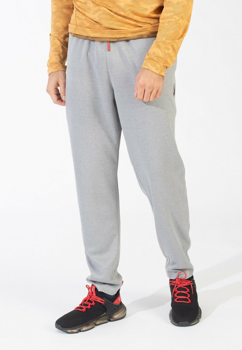 Grå sweatpants med elastisk talje, sidelommer og et lille logo. Båret sammen med sorte sneakers med røde snørebånd og detaljer.