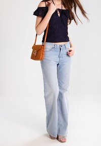 Top corto de encaje navy con diseño off-shoulder, combinado con jeans acampanados de color azul claro y un pequeño bolso cruzado naranja. Sandalias ligeras completan el look.
