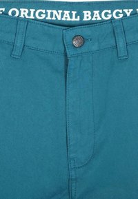Pantaloni baggy color teal con zip e chiusura a bottone, e etichetta ricamata in vita con la scritta "THE ORIGINAL BAGGY." Realizzati in resistente tessuto di cotone.