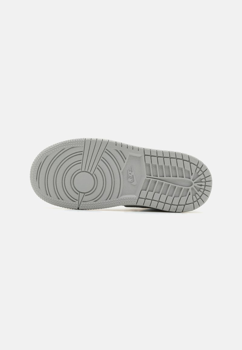 Suela de zapatilla de goma gris con patrones de rodadura circulares y lineales, con una sección circular central y un detalle de logo.