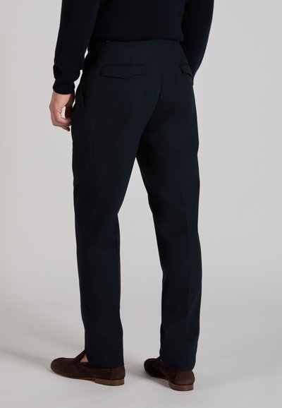 Navy blue tailored trousers, featuring a smooth texture, two back pockets, and a straight-leg design, paired with brown suede loafers.