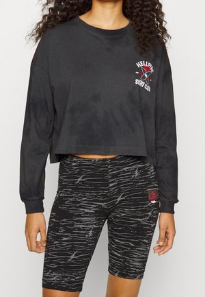 Sort kortærmet langærmet skjorte med logo og grå leggings med mønster. Begge er lavet af blødt, elastisk stof med en glat tekstur.