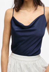 Navy Satin-Cami mit einem Schößchen-Ausschnitt, dünnen Trägern und glatter Textur, kombiniert mit einem leichten, gerafften weißen Rock.