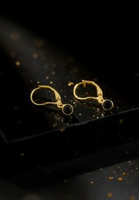 Orecchini a cerchio in oro con un gemstone nero circolare incastonato in una montatura a punte, dal finish liscio e lucido e con chiusura a cerniera.