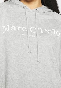 Szara bluza z kapturem wykonana z miękkiego materiału, z troczkiem w kapturze, z napisem "Marc O'Polo" w białym kolorze na klatce piersiowej oraz akcentami w ściągaczu.