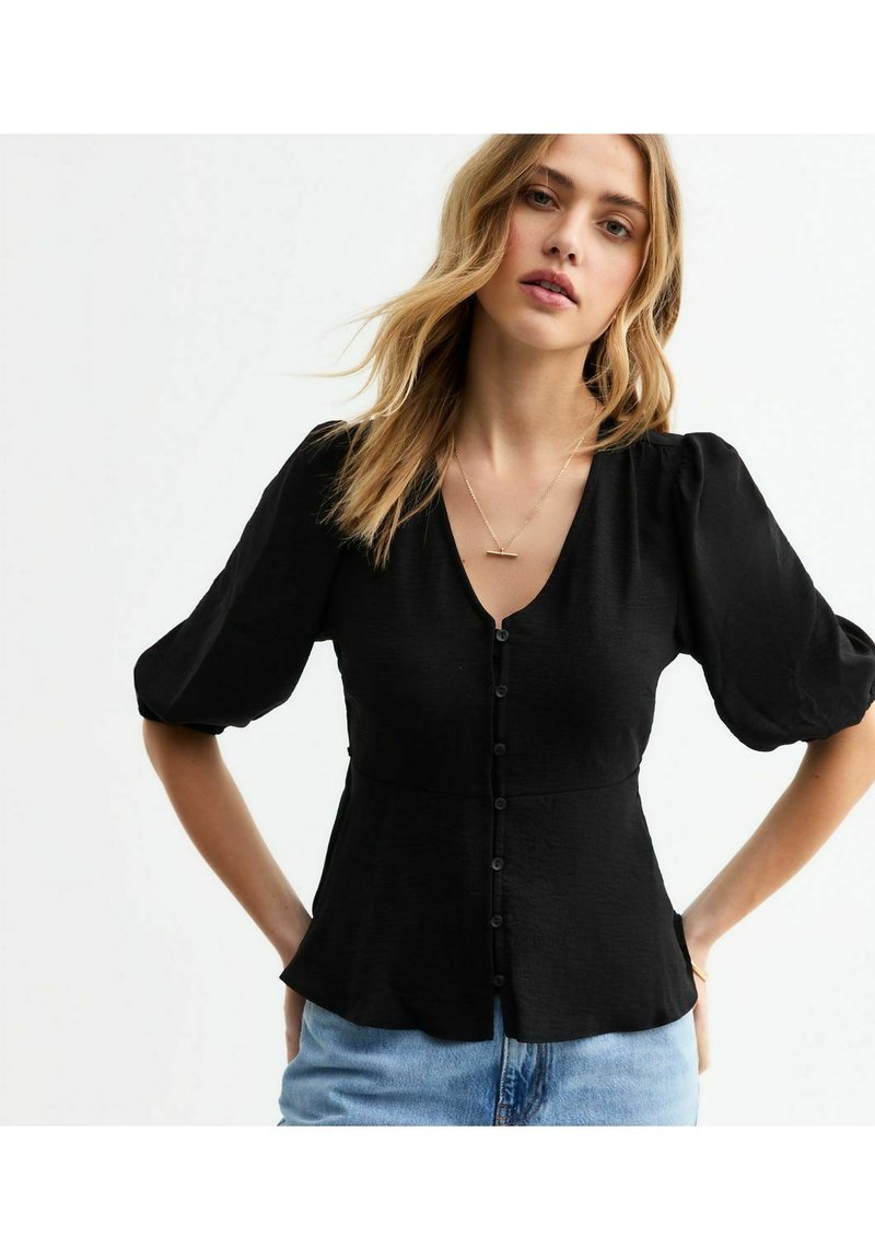 Svart, knapp-up blus med V-ringning, puffärmar och en peplum midjedesign. Mjuk textur, avslappnad stil, kombinerad med blå denim.