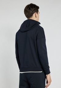Granatowy hoodie wykonany z miękkiego materiału, z kapturem, prążkowanymi mankietami i luźnym krojem. Gładka tekstura z minimalnymi detalami.