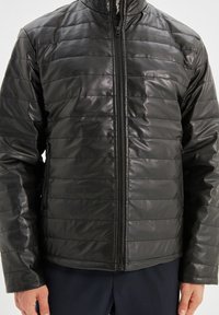 Giacca imbottita nera realizzata in materiale lucido e trapuntato, con colletto alto e zip frontale. Le cuciture orizzontali creano un design strutturato.