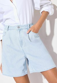 Light blue denim shorts with a high waist, featuring a front button closure, belt loops, and side pockets. Smooth, casual design.