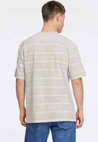 Camisa de manga corta a rayas beige con una tela texturizada, que presenta un escote redondo y un corte recto, combinada con unos jeans de mezclilla azules.