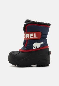 Marineblaue Winterstiefel mit schwarzer Gummisohle, roten Akzenten, gefüttertem Innenfutter aus Fell und einem weißen Bärenmotiv. Klettverschluss mit eingedrucktem Markennamen.