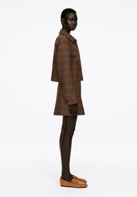 Brown plaid, cropped jacket with a collar and button closure, paired with a matching skirt. Brown suede loafers complete the look.