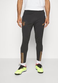 Svarta idrottsbyxor med elastisk midja, prydda med en gyllene Tyskland-logga och tre gyllene ränder på sidan, tillverkade av ett slätt tyg.