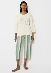 Kremowa bluzka z długim rękawem z kwiatowym wzorem; jasnoniebieskie i białe paskowane spodnie w kroju cropped. Miękka tkanina, luźny krój, swobodny styl.