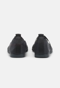 Scarpe nere slip-on con tomaia in tessuto liscio, dettagli con fascette elastiche e suola piatta in gomma. Due asole posizionate sul retro.