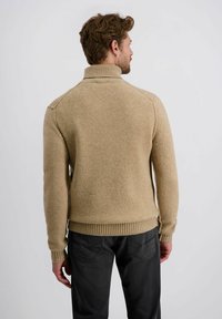 Beige Strickpullover mit hohem Kragen und geripptem Saum. Verfügt über einen strukturierten Stoff und eine taillierte Silhouette. Getragen mit dunklen Hosen.
