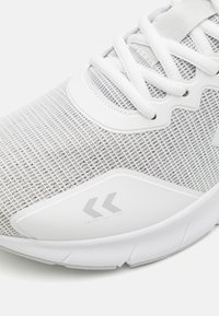 Białe buty sportowe z przewiewną siateczkową cholewką, teksturowanymi detalami i gumową podeszwą. Zawierają logo marki oraz akcent w okolicy palców.