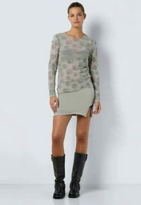 Long-sleeve, gray top with floral pattern; paired with a light green skirt featuring a side slit. Model wears knee-high black boots.
