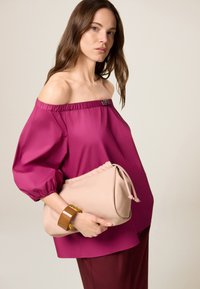 Off-Shoulder Fuchsia Top mit elastischem Kragen, kombiniert mit einer beigen Clutch und einem klobigen braunen Armband. Glattes Material, lockere Passform.