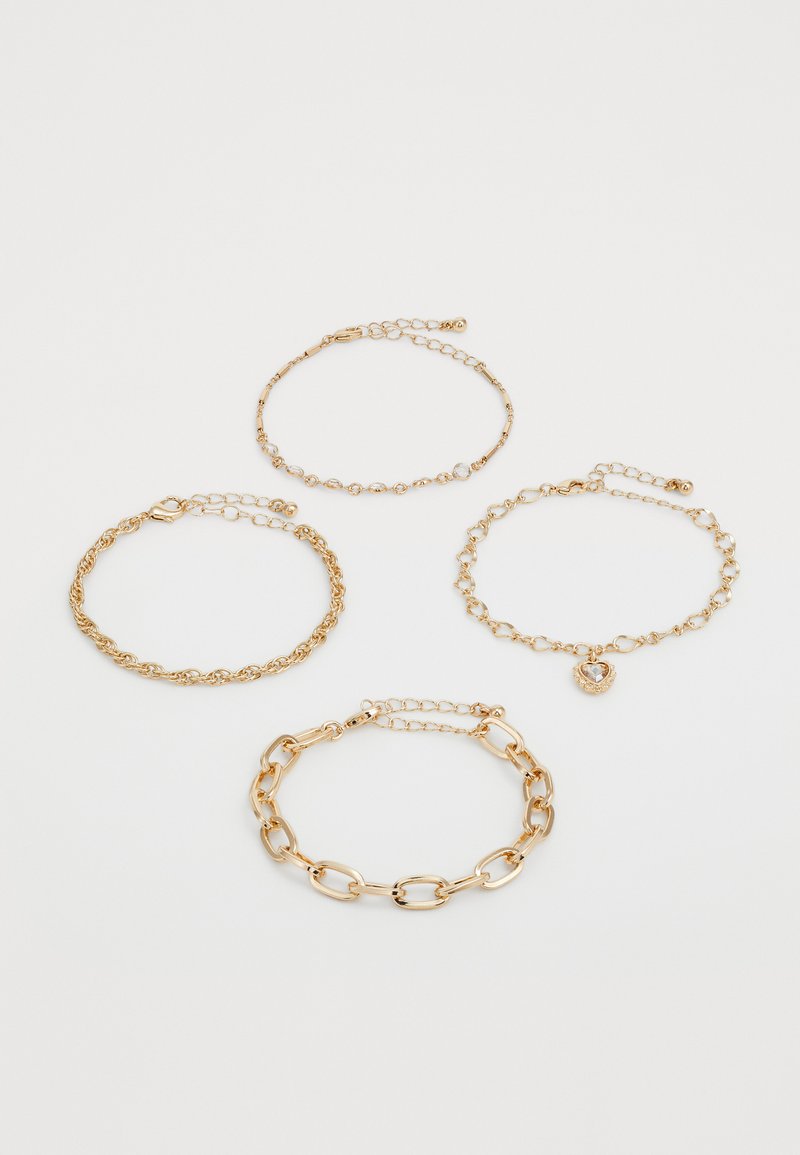 Quatro delicadas pulseiras de corrente em ouro com estilos de elos variados, uma delas apresentando um charme em forma de coração com uma gemas transparente.