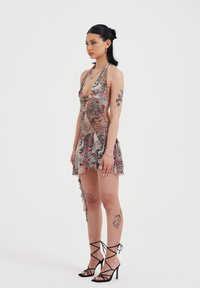 Vestido de tirantes con estampado floral, escote en V profundo, dobladillo asimétrico y acentos con volantes, fabricado en una tela ligera y texturizada. Tacones negros con tiras.