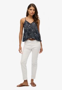 Camisole w marynarskie wzory z cienkimi ramiączkami i rozkloszowanym fasonem, w połączeniu z białymi spodniami slim-fit i brązowymi klapkami.