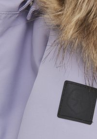 Ljuslila jacka av tyg med texturerad yta, med en fuskpälskrage och ett distinkt svart logopatch.