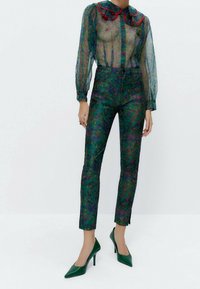 Przezroczysta zielona bluzka z czerwoną kołnierzykiem, w połączeniu z jeansami o wysokim stanie z kwiecistym wzorem w odcieniach zieleni, czerwieni i niebieskiego. Zielone szpilki.