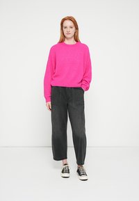 Pulover fucsia tricotat cu gât rotund, asortat cu blugi negri evazați și adidași negri cu talpă albă.